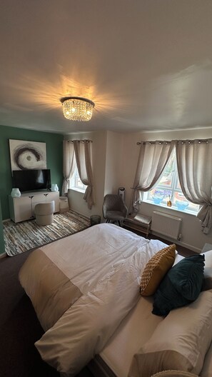 A hotel room with a large bed, a television, a chair, and a window with curtains. - Cosy 3 bedroom home close to Wembley Stadium, Heathrow & Luton! (Borehamwood)