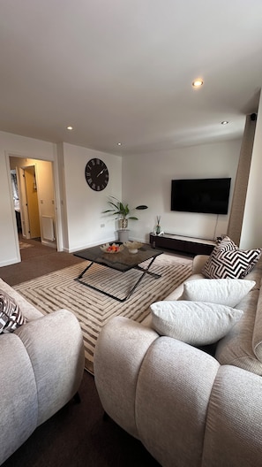 A modern living room with a sofa, a coffee table, a wall clock, and a flat-screen TV.