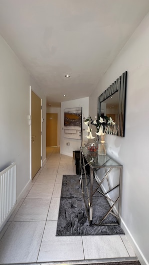 A hallway with a glass coffee table, a mirror, and a door leading to another room. - Cosy 3 bedroom home close to Wembley Stadium, Heathrow & Luton! (Borehamwood)