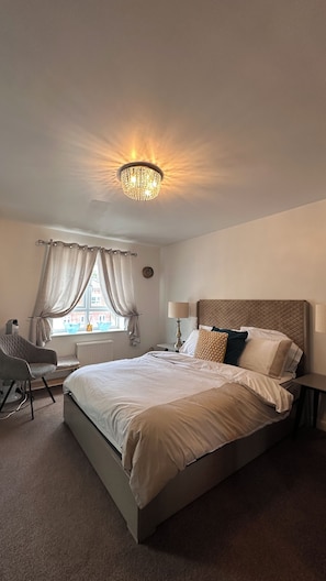 A hotel room with a bed, a chair, a lamp, and a window with curtains.