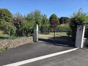 Una entrada cerrada con un cerramiento de metal, un camino pavimentado y un muro de piedra.