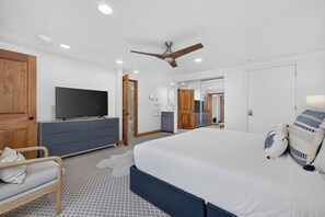 A modern bedroom with a large bed, a television, a ceiling fan, and a bathroom visible through an open door. - Charter Ski In Ski Out 2BR (Avon)