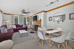 A living room with a sofa, a dining table with chairs, a fireplace, and a ceiling fan. - Charter Ski In Ski Out 2BR (Avon)