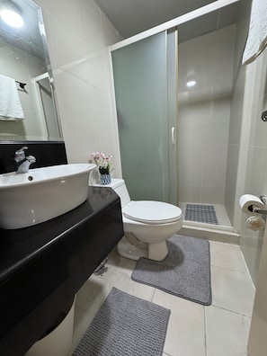 Ein Badezimmer mit einem weißen Waschbecken, einer Toilette, einer Duschkabine mit Glastür und einer kleinen Pflanze auf der Ablagefläche.