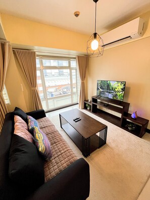 Ein Wohnzimmer mit einer Couch, einem Couchtisch, einem Fernseher und einem Fenster mit Vorhängen.