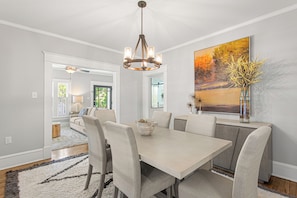 A dining area with a light-colored table and chairs, a chandelier, and a large painting on the wall. - The Hamilton a Stylish Downtown Bungalow (High Point)