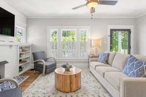 A living room with a fireplace, a sofa, a chair, a coffee table, and a ceiling fan. - The Hamilton a Stylish Downtown Bungalow (High Point)