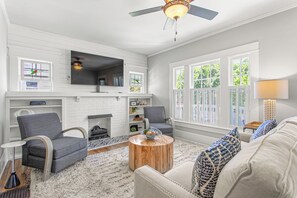 A living room with a fireplace, a ceiling fan, and large windows. - The Hamilton a Stylish Downtown Bungalow (High Point)