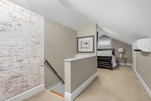 A bedroom with a sloped ceiling, a bed, a bedside table with a lamp, and a framed picture on the wall. - The Hamilton a Stylish Downtown Bungalow (High Point)