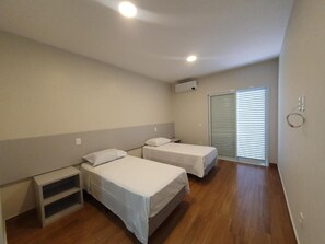 A bedroom with two beds, a window with blinds, and an air conditioning unit. - Pousada Thermas das Montanhas (Aguas de Lindoia)