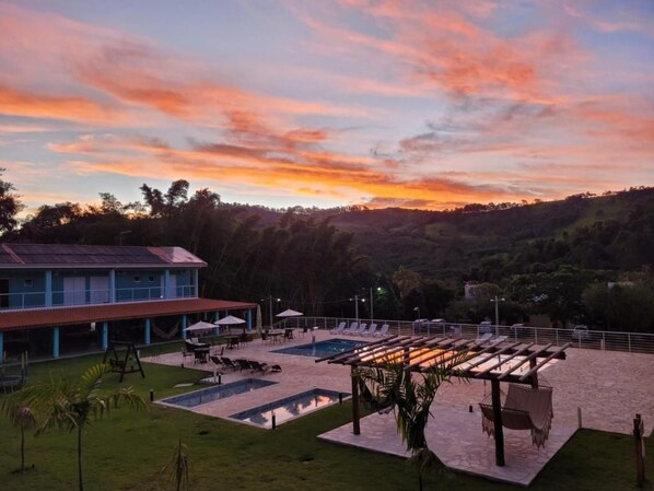 A resort with a swimming pool, lounge chairs, and a building with a red roof. - Pousada Thermas das Montanhas (Aguas de Lindoia)