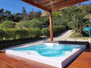 A hot tub on a wooden deck with a pergola overhead, surrounded by lush greenery and a hillside in the background. - Pousada Thermas das Montanhas (Aguas de Lindoia)
