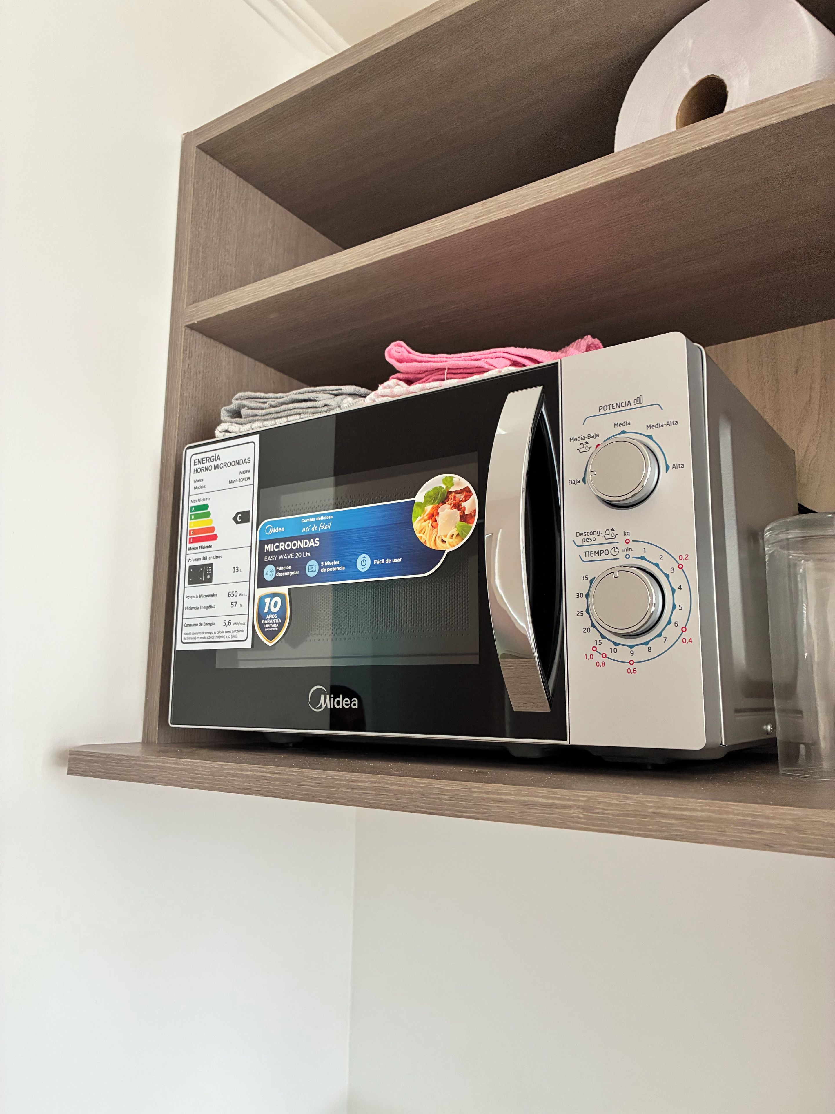 Un four à micro-ondes posé sur une étagère en bois, doté d’un écran numérique, d’un bouton de réglage de la puissance et d’un récipient en verre à proximité.