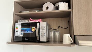 Una cocina con un microondas en un estante de madera, un rollo de toallas de papel y una taza blanca.