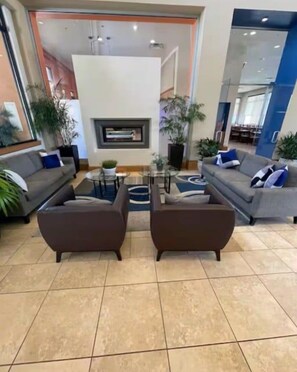 Eine moderne Lobby mit zwei Sofas, die einen Kamin gegenüberhaben, einem Couchtisch und Topfpflanzen.