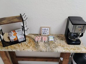 Eine Küchenarbeitsplatte mit einer Kaffeemaschine, einem Becherregal und verpackten Lebensmitteln.