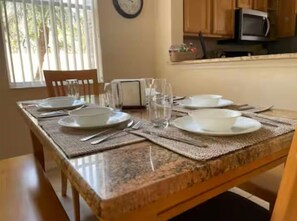 A dining table set with plates, glasses, and cutlery, with a kitchen in the background. - 4BR Townhome Water Slides, heated pool Near Disney, walking distance to Old Town (Kissimmee)