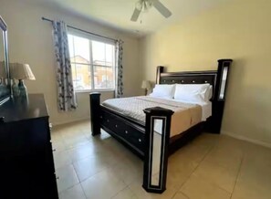 A bedroom with a bed, a nightstand, a dresser, a window with curtains, and a ceiling fan. - 4BR Townhome Water Slides, heated pool Near Disney, walking distance to Old Town (Kissimmee)
