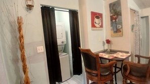 A small dining area with a table and chairs, a wall-mounted light fixture, and a door with a curtain. - Charming Efficiency unit in enjoyable Ormond Beach House with Tropical Garden (Ormond Beach)