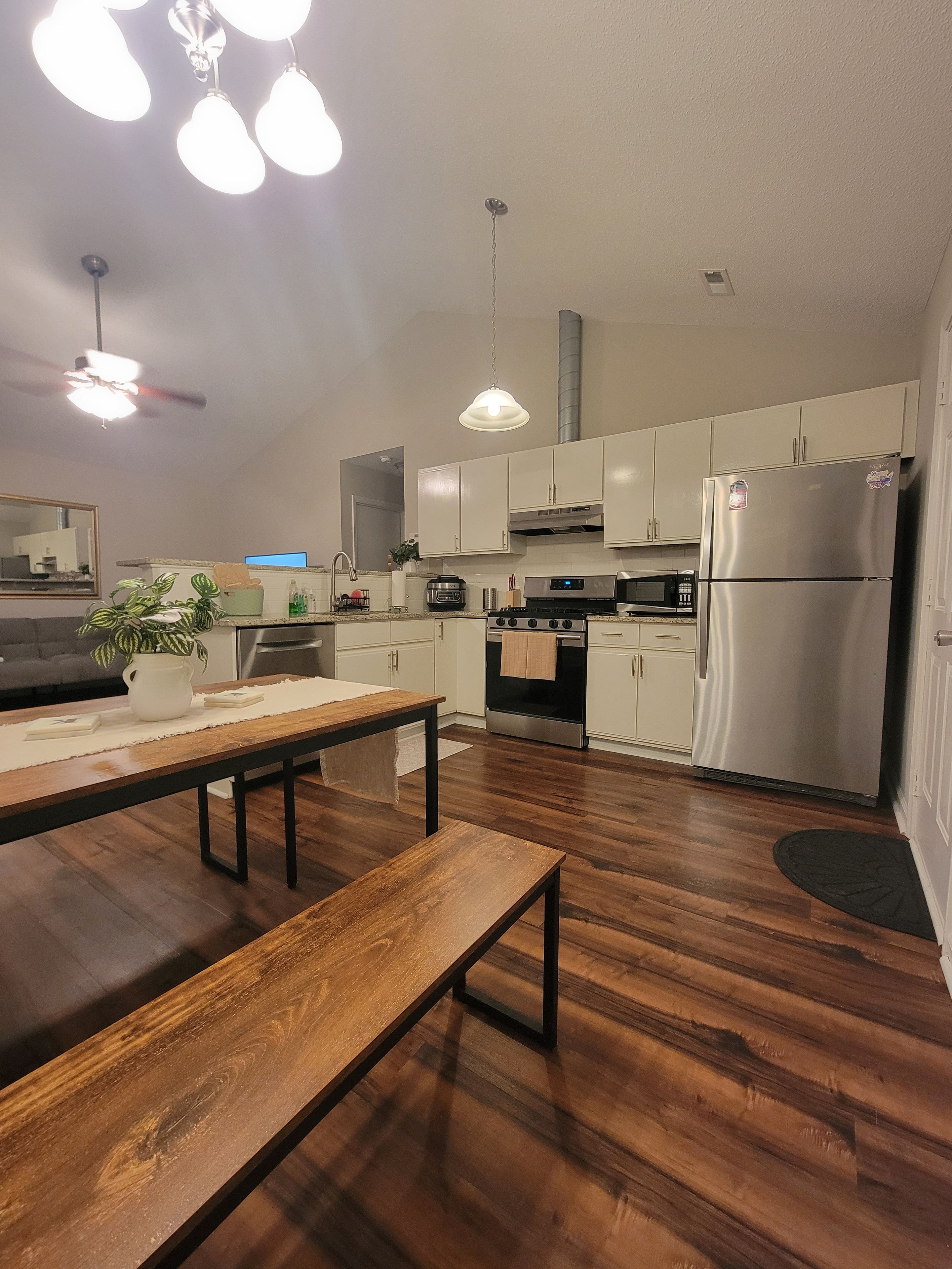 A modern kitchen with wooden flooring, white cabinets, stainless steel appliances, and pendant lighting.