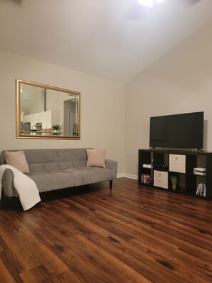 Ein Wohnzimmer mit einem grauen Sofa, einem Fernseher auf einem schwarzen Schrank und einem Spiegel an der Wand.