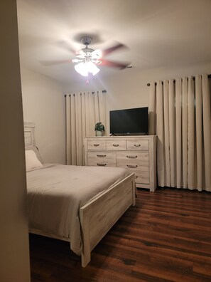 Un dormitorio con cama, cómoda, televisor y ventilador de techo.