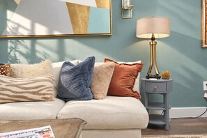Ein Wohnzimmer mit einer Couch, dekorativen Kissen, einem Beistelltisch mit Lampe und einem Wandbild.