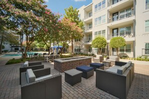 An outdoor patio area with wicker furniture, a brick fire pit, and a swimming pool. - The Bentley Collection - The Blue Ivy (Dallas)