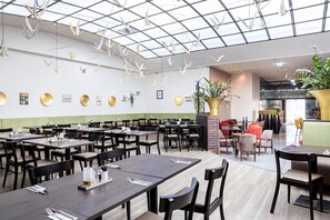 En moderne restaurant med flere spiseborde og stole, et glasloft og dekorativ vægkunst.
