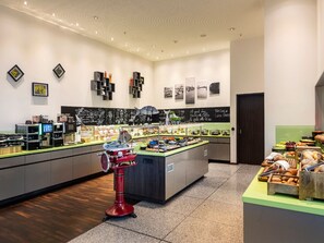 Ein modernes Café mit einer zentralen Theke, verschiedenen Speisenpräsentationen und einer Kreidetafel-Speisekarte.