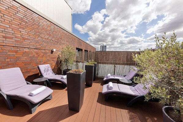 Eine Dachterrasse mit Lounge-Möbeln, Blumentöpfen und einem Holzzaun.