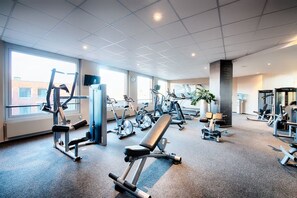 Ein Fitnessraum mit unterschiedlichen Trainingsgeräten, großen Fenstern und einer Sitzbank.