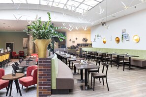 En moderne restaurant med et buet siddeområde, en stor planteinstallation og et højt loft med hængende lysarmaturer.