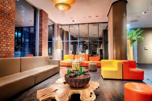 En moderne lobby med en murstensvæg, et stort træbord og orange og beige siddepladser.