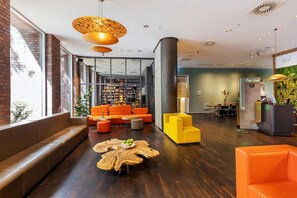 En moderne lobby med en murstensvæg, en stor reol, orange siddemøbler og en reception.