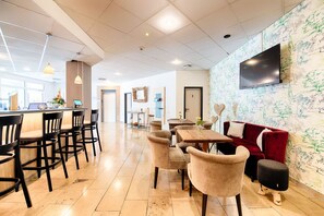 Eine moderne Hotelhalle mit Barbereich, Sitzgelegenheiten und einem an der Wand montierten Fernseher.