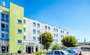 Ein modernes Gebäude mit einer grün-weißen Fassade, zahlreichen Fenstern und einem gut sichtbaren Eingang.