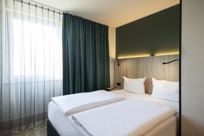 Ein Hotelzimmer mit Bett, Nachttisch, Lampe und einem Vorhangfenster.