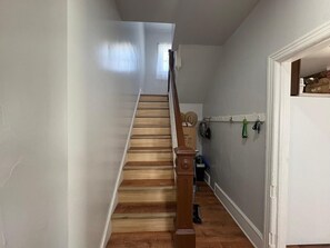 Eine Treppe mit Holzdielen und einer Handläufe führt zu einem Raum mit einer weißen Tür, einem Kleiderhaken mit Schlüsseln und einer Tasche.