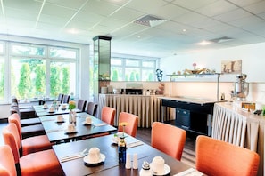 Ein Hotelrestaurant mit mehreren Tischen, Stühlen und einer Küche im Hintergrund.