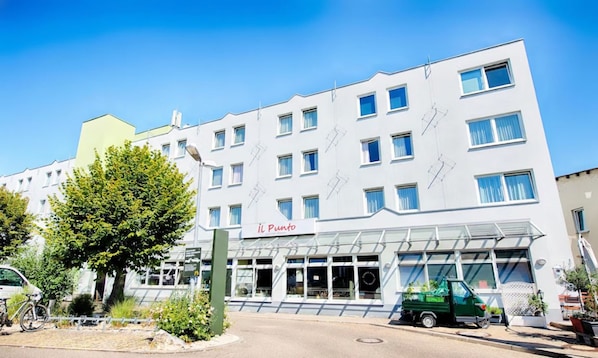 Ein mehrstöckiges Hotel mit moderner Fassade, davor ein grüner Lastwagen, und ein klarer, blauer Himmel.