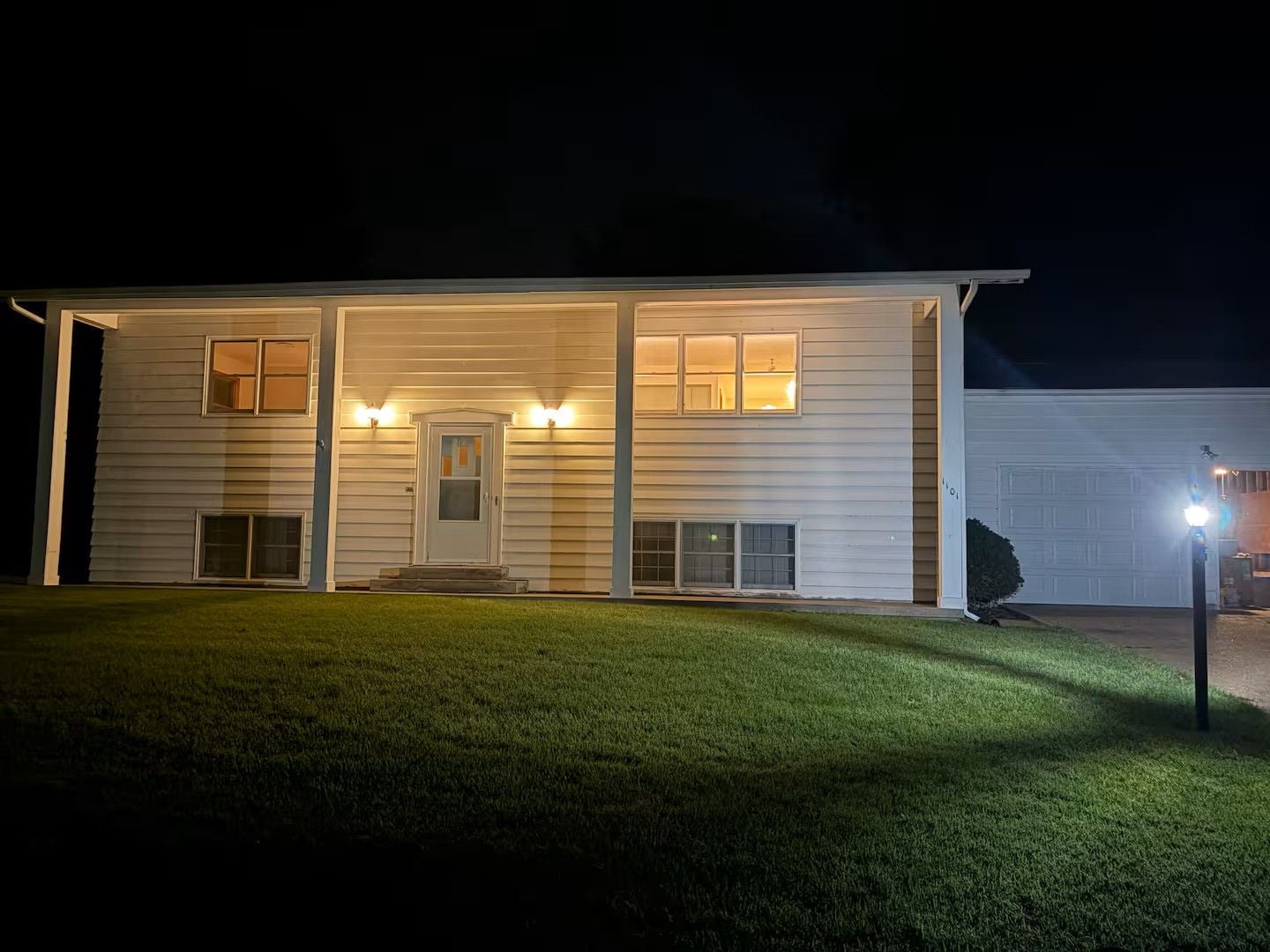 Una casa a due piani con un portico, un garage e un esterno ben illuminato.