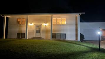 Una casa a due piani con un portico, un garage e un esterno ben illuminato.