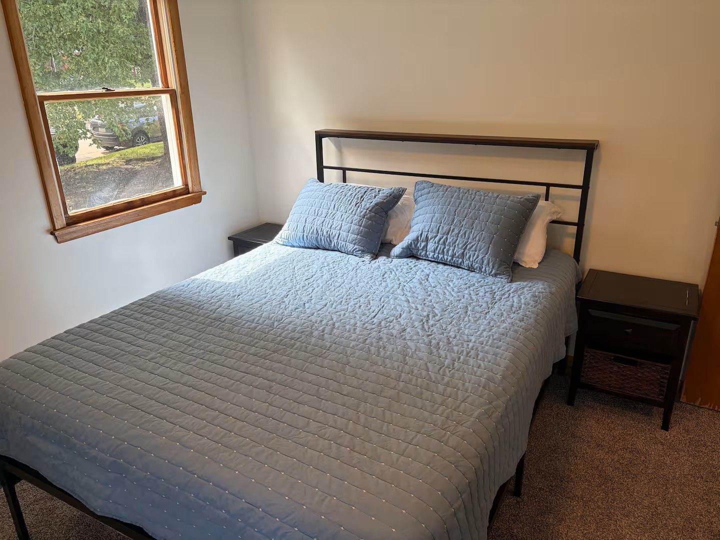 Una camera da letto con un letto, due comodini, una finestra e vista su del verde all'esterno.