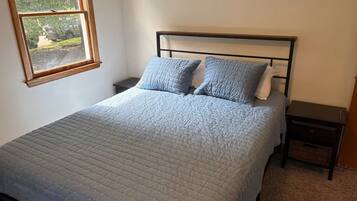 Una camera da letto con un letto, due comodini, una finestra e vista su del verde all'esterno.