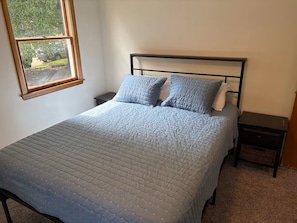 Una camera da letto con un letto, due comodini, una finestra e vista su del verde all'esterno.