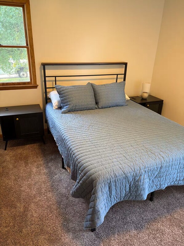 A bedroom with a bed, two nightstands, a window, and a lamp.