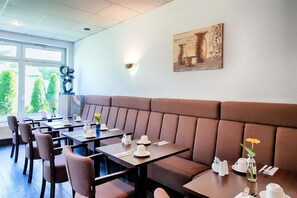 Ein Restaurant mit einer langen Sitzbank, Tischen mit Stühlen und einem großen Fenster mit Blick auf Grünflächen.