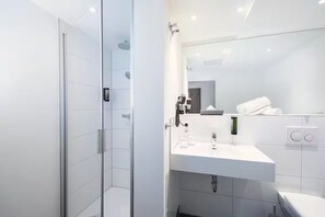 Ein modernes Badezimmer mit Duschkabine aus Glas, einem weißen Waschbecken mit Spiegel und einer Toilette.