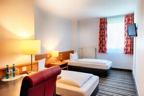 Ein Hotelzimmer mit zwei Betten, einem roten Sessel, einem Fernseher und einem fenster mit Vorhängen.